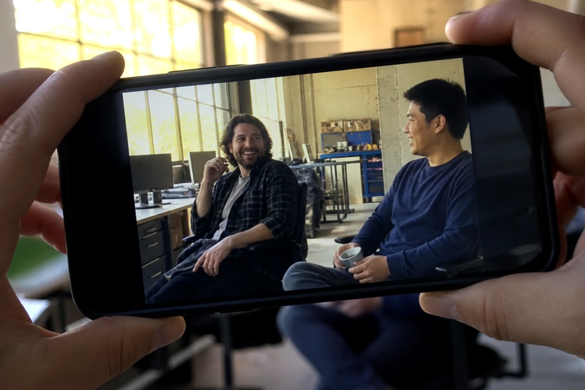 Two coworkers at a desk filming a product on a phone